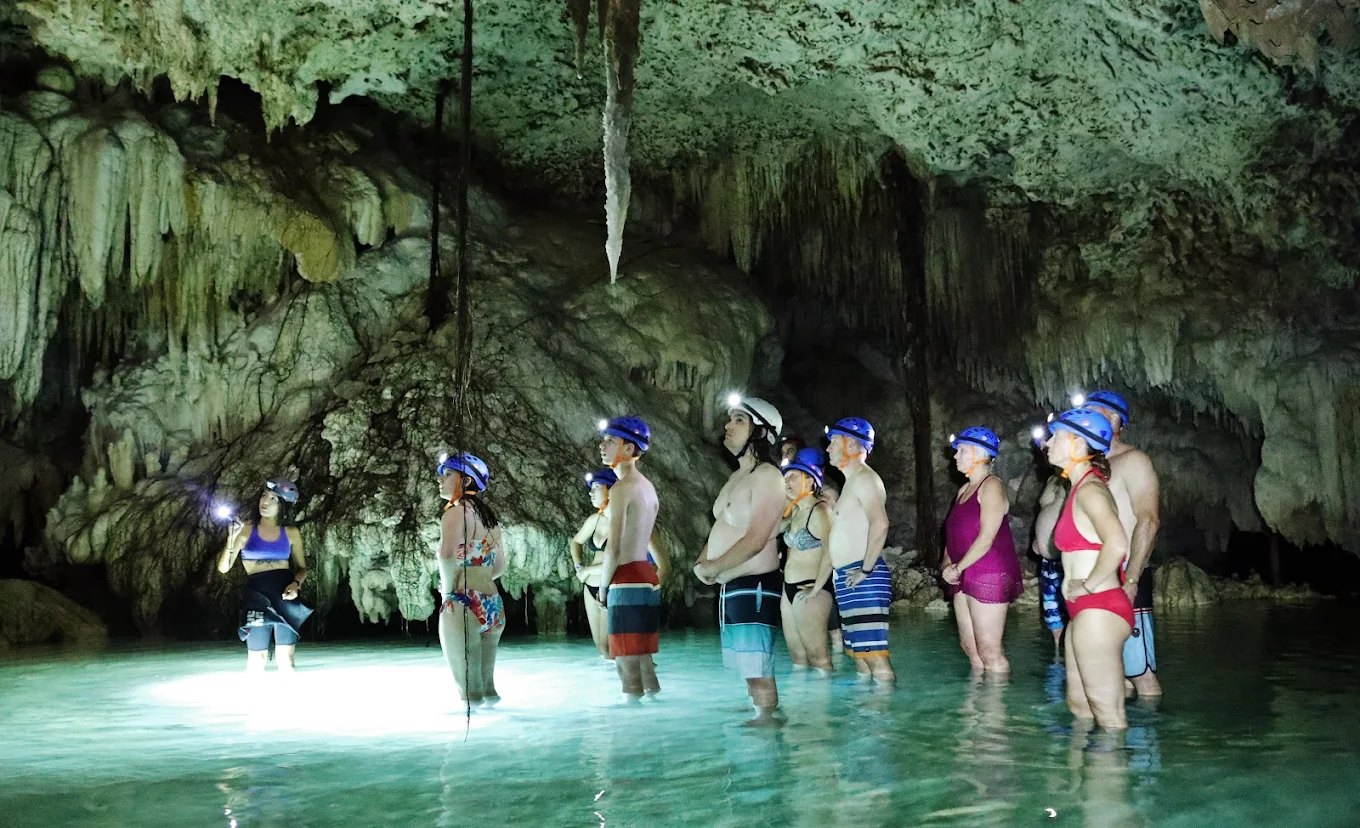 Grupo de viajeros con casco dentro de un cenote de caverna con estalactitas