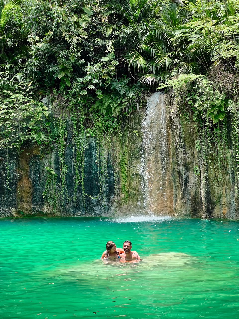 Pareja bañándose bajo una pequeña cascada en un cenote de Tulum
