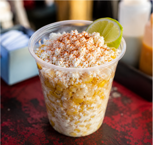 Vaso de esquites con queso, chile y lima en un puesto