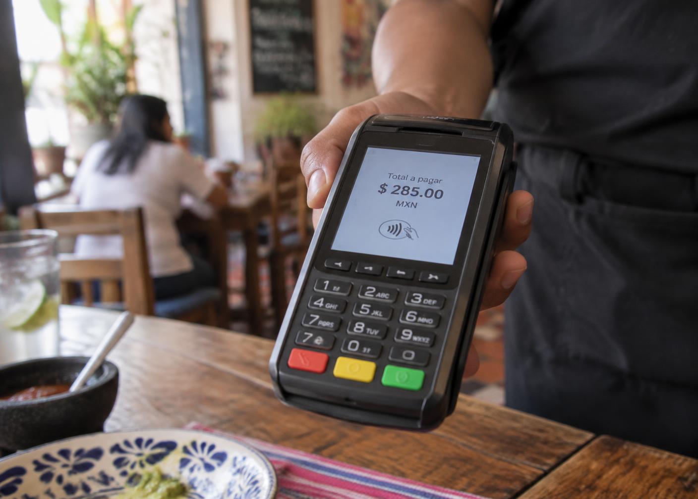 Datáfono mostrando un importe en pesos mexicanos en un restaurante